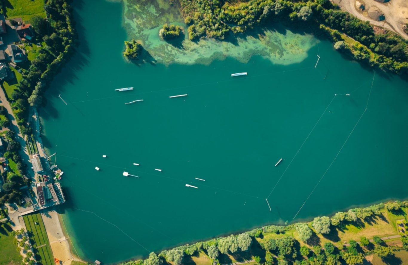 Wakepark Pfullendorf Vogelperspektive auf einen klaren See mit einer Wakeboardanlage und umgebenden grünen Uferlandschaften.